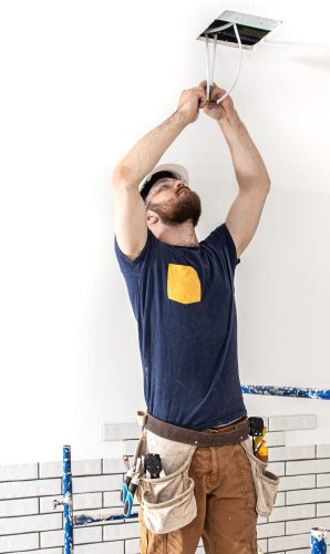 Electrician Builder at work, installation of lamps at height. Professional in overalls with an electrical tool. On the background of the repair site. The concept of working as a professional.